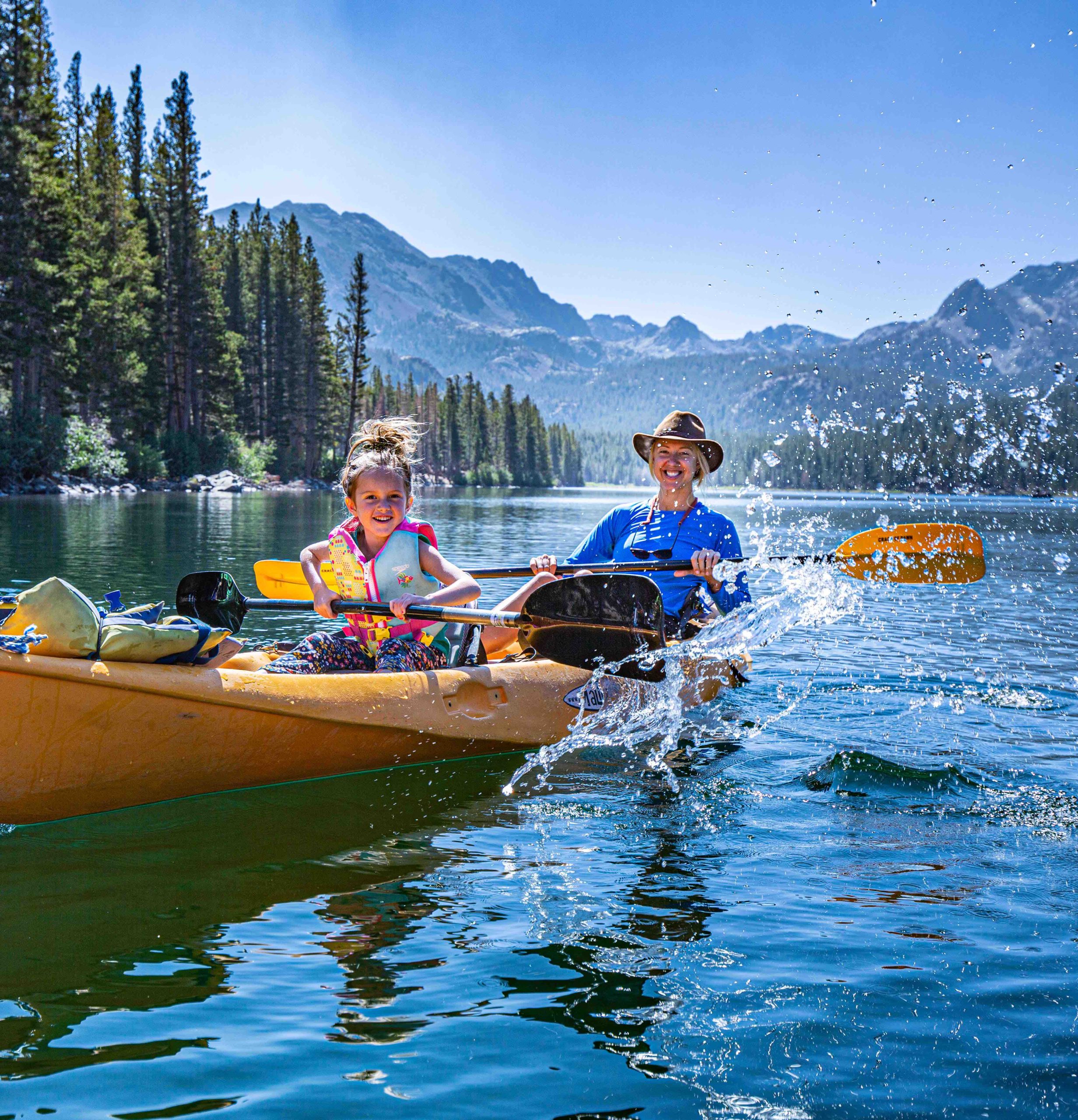 A mother and daughter paddling a kayak on an alpine lake in Mammoth Lakes, the Sierra Nevada rising behind them